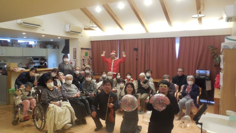 介護施設でのレクリエーション。入居者と職員が楽器演奏や風船を使った活動を楽しんでいます。